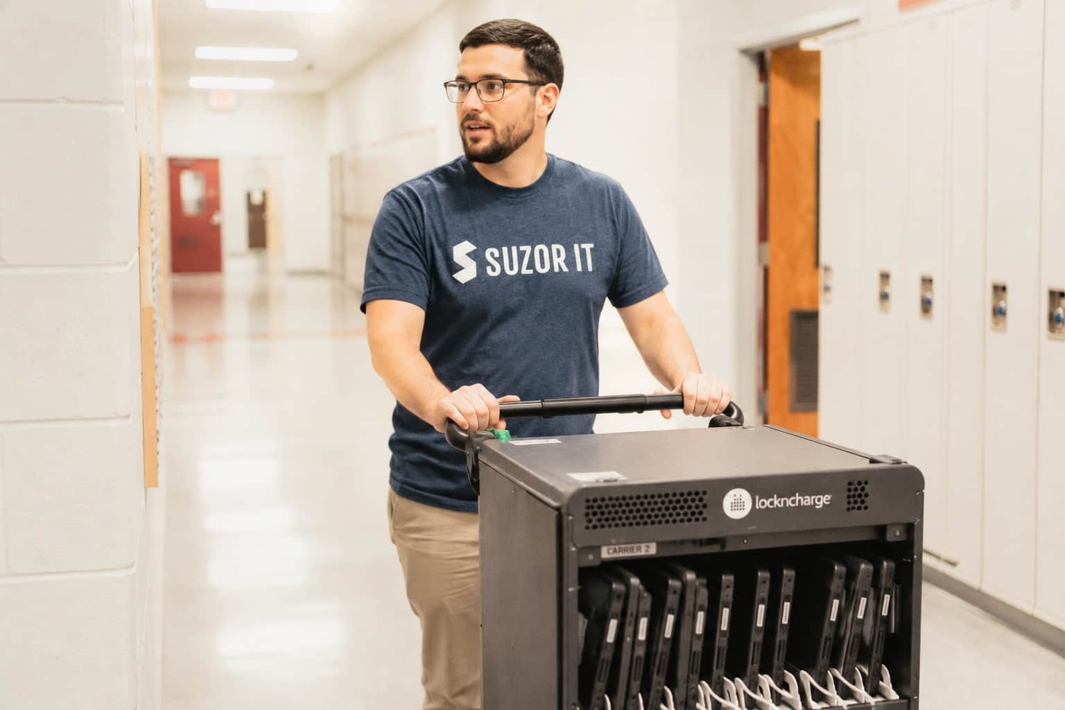 Technician wheeling a Chromebook cart down a school hallway