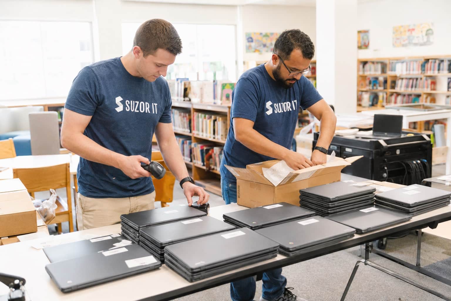 Technicians asset-tagging Chromebooks in a school library